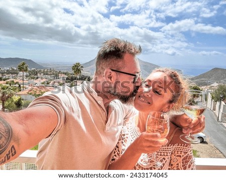 One happy adult couple taking selfie picture at home in terrace with city and mountains outdoors view. People enjoying vacation and leisure together smiling and drinking wine. Joyful people holiday