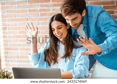 Happy young couple say hallo during videocall at home using laptop. Modern people meet friends in chat online conference on computer with internet connection. Greet friends. Small business freelance Royalty-Free Stock Photo #2433174069