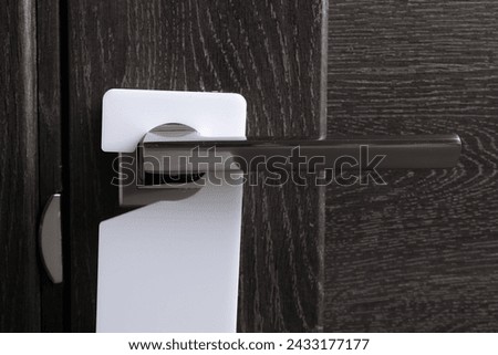 Closed wooden door with blank hanger on metal handle, closeup