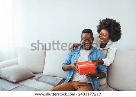 African descent brazilian couple exchanging gifts at home. Surprised woman receiving Birthday present from her boyfriend. Young happy woman being surprised by her boyfriend with a birthday preset. 