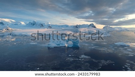 Aerial view of frozen Antarctica iceberg arch float in icy ocean. Glacier under sunset sky, mountains in background. Antarctic travel and exploration. Beauty of wild untouched nature. Drone panorama
