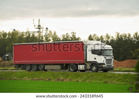Modern white trucks with semi-trailers drive on a highway. Transporting cargo containers for commercial and industrial purposes. Sustainable logistics and efficient delivery methods to ship goods. Royalty-Free Stock Photo #2433189645