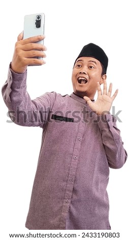 Happy asian Muslim man greeting at the smartphone during video call, happy indonesian muslim man holding smartphone and greeting to someone during video call, ramadan and eid mubarak celebration. 