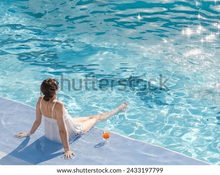 Cute woman with a glass of drink sits near the swimming pool of a cruise ship. Sunny, clear morning. View from above. Closeup, outdoors. Vacation and travel concept