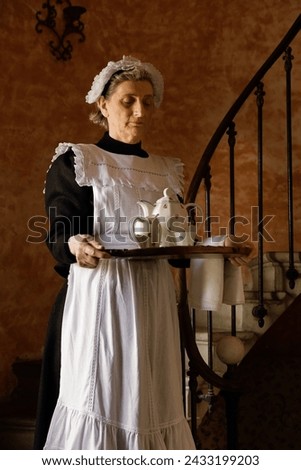 Victorian maid or servant in black dress, lace cap and white apron working in a 19th century interior Royalty-Free Stock Photo #2433199203