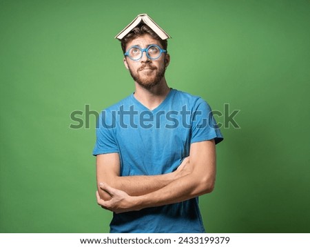 Nerdy man with quirky expression balancing book on head - Concept of unconventional learning methods.
