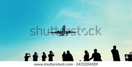 Silhouette of group of unknown people tourists take pictures a landing passenger airplane flying in blue sky background