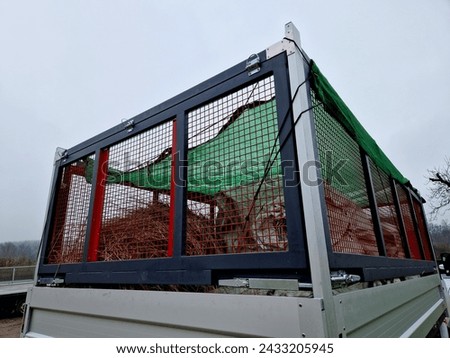 properly covered pile of cut grass from garden maintenance on a trailer with a lattice superstructure for a larger capacity of the truck. gardening services, cage, net, green, foil, tarpaulin, textile Royalty-Free Stock Photo #2433205945