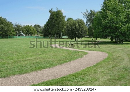 Scenic view of a winding stone walkway through a beautiful spacious park garden with green leafy trees, a mowed grass lawn and clear blue sky above Royalty-Free Stock Photo #2433209247