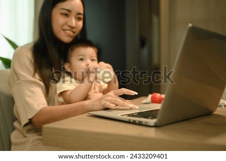 Cropped shot mother working with laptop at home with little baby son. Motherhood and child care concept