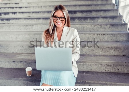 Shot of a young businesswoman using a laptop on the stairs against a city background