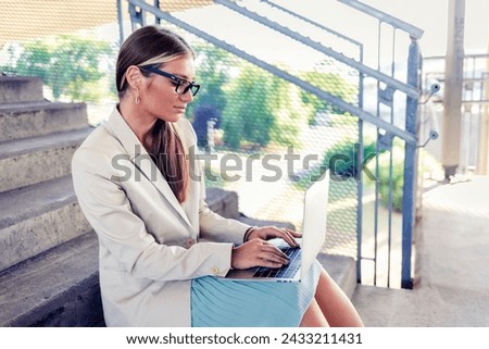 Woman sitting on steps outdoors and using laptop. Businesswoman working on laptop while sitting on steps outside.