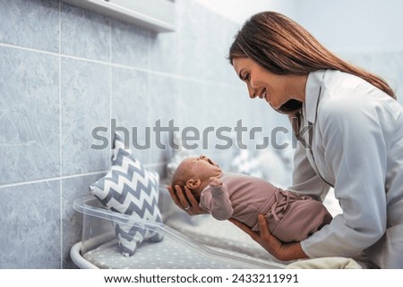 White female doctor or nurse is holding small infant. Newborn baby in hospital at neonatal resuscitation center with nurse. Maternity hospital, doctor and nurse neonatologist Royalty-Free Stock Photo #2433211991