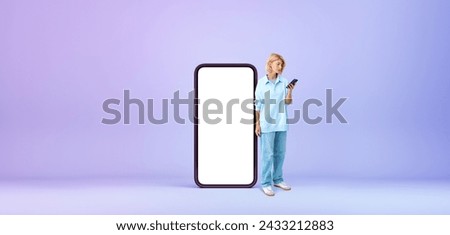 Beautiful European woman standing near big smartphone with mock up display over purple background. Concept of communication and advertisement