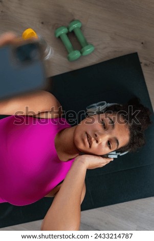 Woman resting after home workout, taking selfie. New Year's resolutions, healthy lifestyle, losing weight and selfcare. Concept of morning or evening exercise. Royalty-Free Stock Photo #2433214787