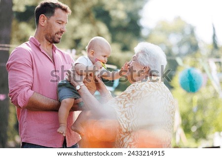 Great-grandmother holding little baby in her arms. Family summer garden party. Royalty-Free Stock Photo #2433214915