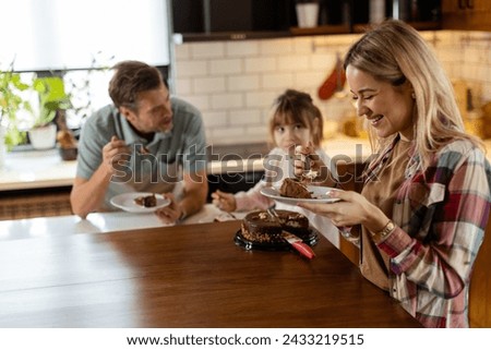 A heartwarming scene unfolds as a family relishes a mouthwatering chocolate cake together in the warmth of their sunlit kitchen, sharing smiles and creating memories Royalty-Free Stock Photo #2433219515