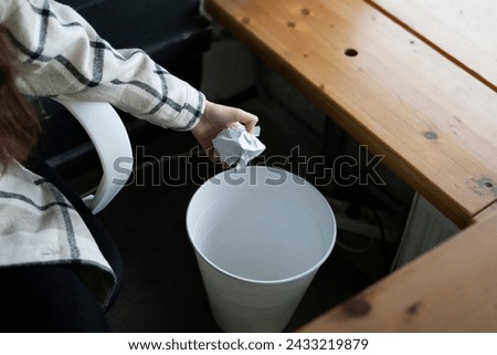 Woman Disposing of Paper Waste in a Small Trash Bin at Her Office Desk Royalty-Free Stock Photo #2433219879