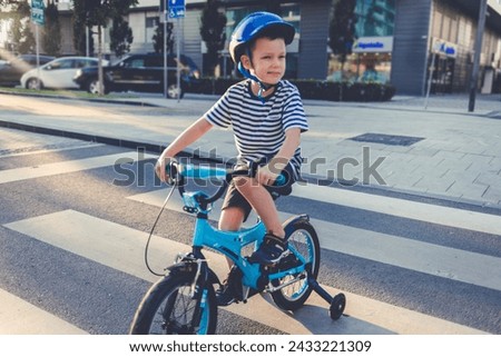 Little boy crossing the street while being on a bicycle. Kid on bicycle waiting for traffic lights on zebra crossing.