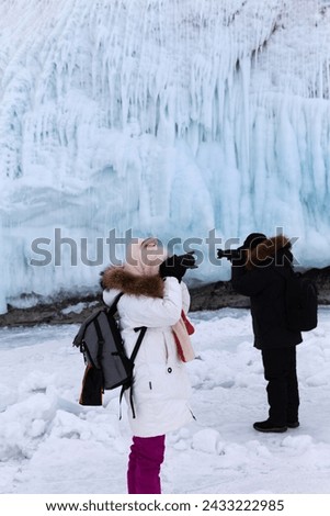 Baikal Lake in winter. Cape Sagan-Khushun or Three Brothers Cliffs are famous among tourists for their ice crusts and huge icicles of bizarre shape. Tourists take pictures of icy rock. Winter outdoors