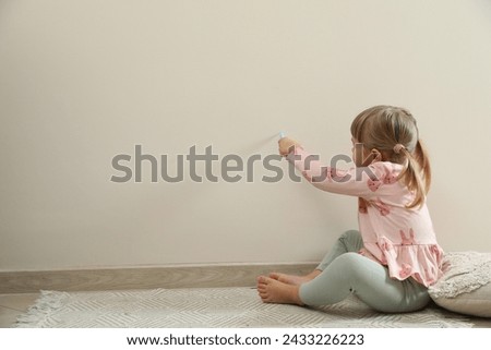 Little girl drawing on beige wall indoors, space for text. Child`s art