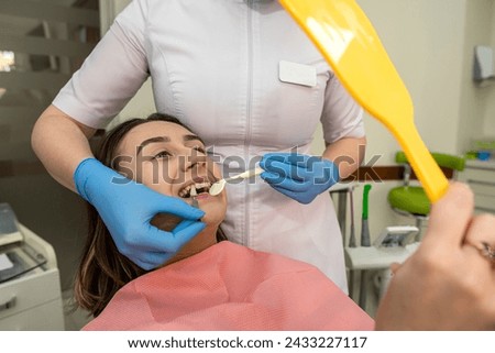 Dentist hold samples for bleaching treatment choosing shade to her patient woman looks in the mirror on result. Teeth whitening, care and hygiene Royalty-Free Stock Photo #2433227117