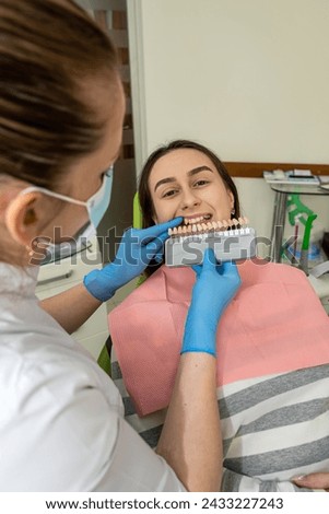 Stomatologist hands holding tooth samples for bleaching treatment female patient, dental procedure for selecting best color of implants  Royalty-Free Stock Photo #2433227243
