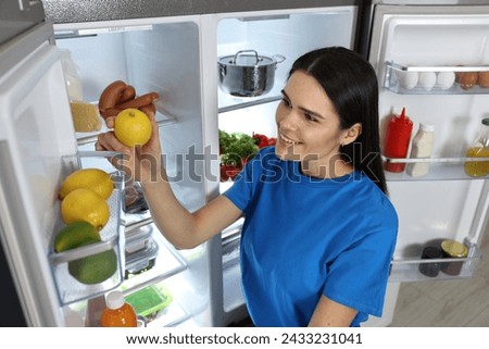 Young woman taking lemon out of refrigerator indoors