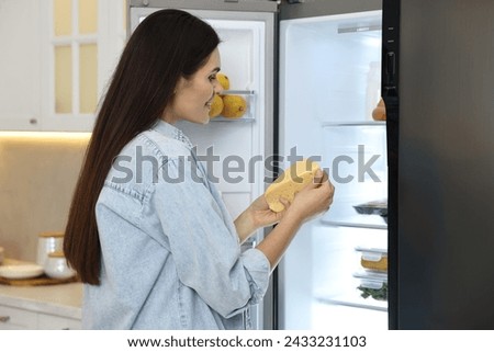 Young woman taking cheese out of refrigerator in kitchen