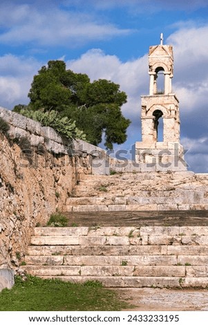 Bell tower of Greek orthodox Church of Panaghia Mesosporitissa on the ruins of ancient sanctuary at Elefsina. Cloudy sky at background. Vertical shot. Eleusis, Attica, Greece