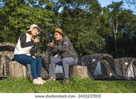 Asian camper man and woman sharing  picture from camera relaxing in front of camping tent in camp site