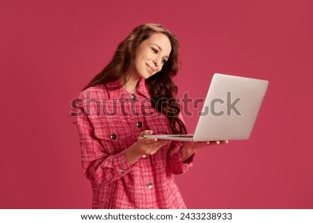 Young beautiful woman holding laptop, working online, doing projects, communicating via Internet against pink studio background. Concept of youth, lifestyle, casual fashion, human emotions