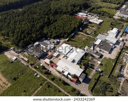 High angle aerial shot capturing an expansive industrial factory complex surrounded by lush greenery and clear skies.