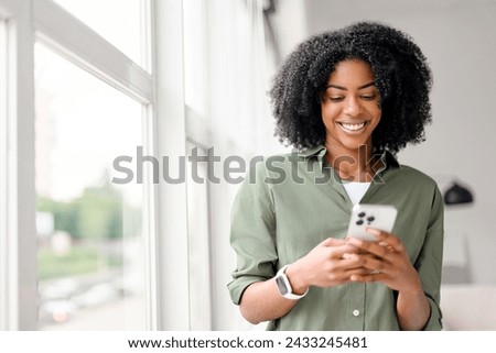 In a well-lit indoor setting, an African-American woman with a contagious smile interacts with her smartphone, engaging with friends or followers through a social network.