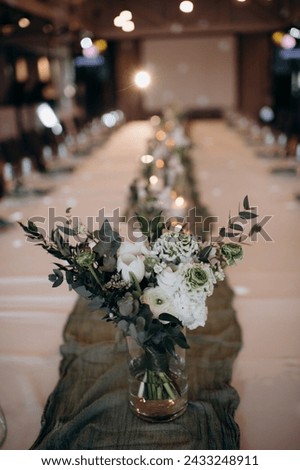 Many small white flower arrangements with roses, eustoma and various flowers in clear glass vases. On the festive table in the wedding banquet area, compositions of flowers and greenery, candles are p Royalty-Free Stock Photo #2433248911