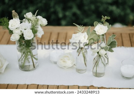 Many small white flower arrangements with roses, eustoma and various flowers in clear glass vases. On the festive table in the wedding banquet area, compositions of flowers and greenery, candles are p Royalty-Free Stock Photo #2433248913