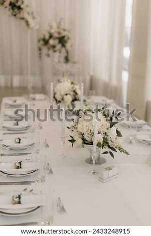 Many small white flower arrangements with roses, eustoma and various flowers in clear glass vases. On the festive table in the wedding banquet area, compositions of flowers and greenery, candles are p Royalty-Free Stock Photo #2433248915