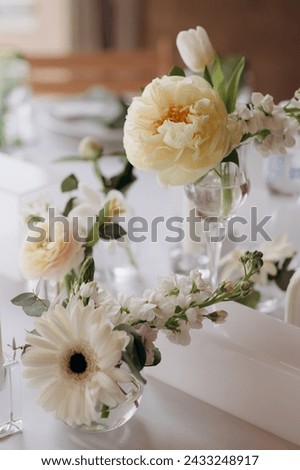 Many small white flower arrangements with roses, eustoma and various flowers in clear glass vases. On the festive table in the wedding banquet area, compositions of flowers and greenery, candles are p Royalty-Free Stock Photo #2433248917