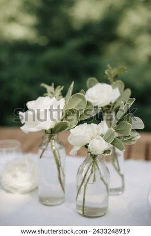 Many small white flower arrangements with roses, eustoma and various flowers in clear glass vases. On the festive table in the wedding banquet area, compositions of flowers and greenery, candles are p Royalty-Free Stock Photo #2433248919