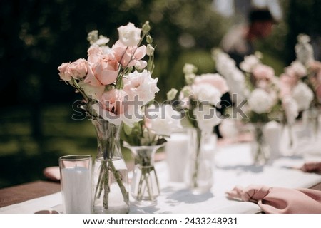 Many small pink and white flower arrangements with roses, eustoma and various flowers in clear glass vases. On the festive table in the wedding banquet area, compositions of flowers and greenery, cand Royalty-Free Stock Photo #2433248931