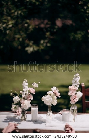 Many small pink and white flower arrangements with roses, eustoma and various flowers in clear glass vases. On the festive table in the wedding banquet area, compositions of flowers and greenery, cand Royalty-Free Stock Photo #2433248933