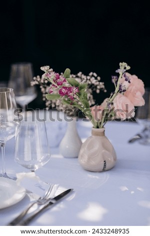 Many small pink and white flower arrangements with roses, eustoma and various flowers in clear glass vases. On the festive table in the wedding banquet area, compositions of flowers and greenery, cand Royalty-Free Stock Photo #2433248935