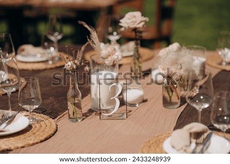 Many small pink and white flower arrangements with roses, eustoma and various flowers in clear glass vases. On the festive table in the wedding banquet area, compositions of flowers and greenery, cand Royalty-Free Stock Photo #2433248939
