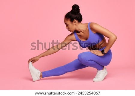 Workout and fitness. Sporty young black lady engages in stretching exercises emphasizing flexibility and muscle tone, doing stretch for hamstring muscles in extended leg squat over pink backdrop Royalty-Free Stock Photo #2433254067