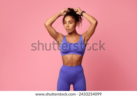 Fitness lifestyle. Motivated African American athletic lady in purple sporty outfit, touching hair making ponytail, preparing for gym workout, standing over pink studio background