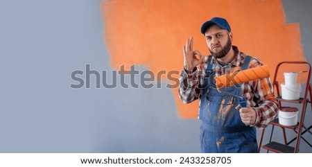 portrait of painter man with paint roller showing ok gesture standing on wall background. Copy space. Banner