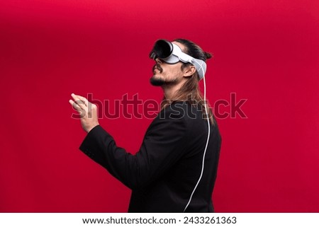 A confident man interacts with an augmented reality environment, showcasing the engaging world of spatial computing and AR and VR technology. Vivid red background Royalty-Free Stock Photo #2433261363