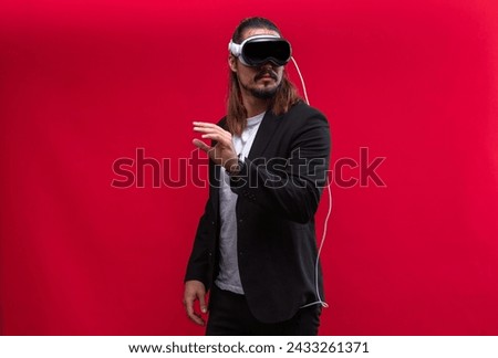 A confident man interacts with an augmented reality environment, showcasing the engaging world of spatial computing and AR and VR technology. Vivid red background Royalty-Free Stock Photo #2433261371
