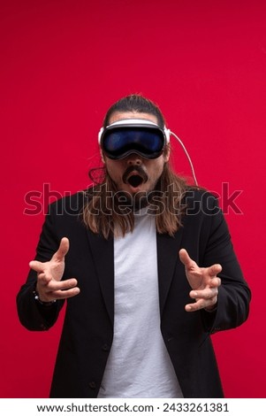 A confident man interacts with an augmented reality environment, showcasing the engaging world of spatial computing and AR and VR technology. Vivid red background Royalty-Free Stock Photo #2433261381