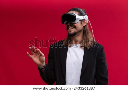 A confident man interacts with an augmented reality environment, showcasing the engaging world of spatial computing and AR and VR technology. Vivid red background Royalty-Free Stock Photo #2433261387
